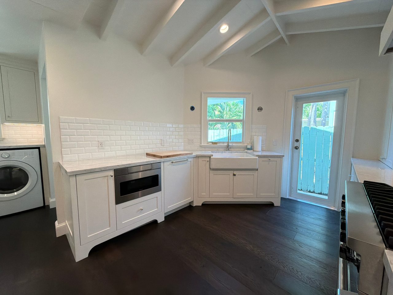 White shaker sink corner with a built-in microwave drawer, panel-front dishwasher, apron sink, beveled tile backsplash, and a glass exterior door