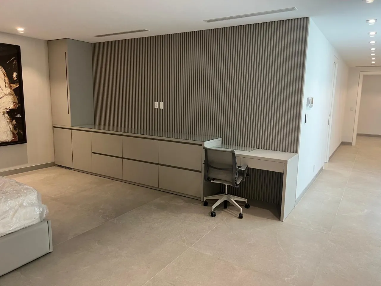 Bedroom desk built into a wall with gray vertical slat accent panel, floating desk and drawer cabinet below, task chair