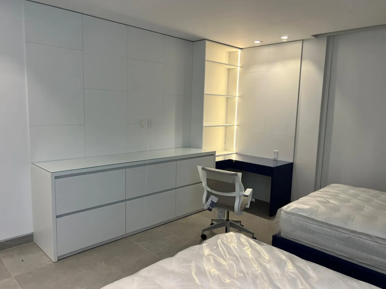 Bedroom with a white built-in wall unit, backlit corner display shelving, and a navy blue floating desk nook beside twin beds
