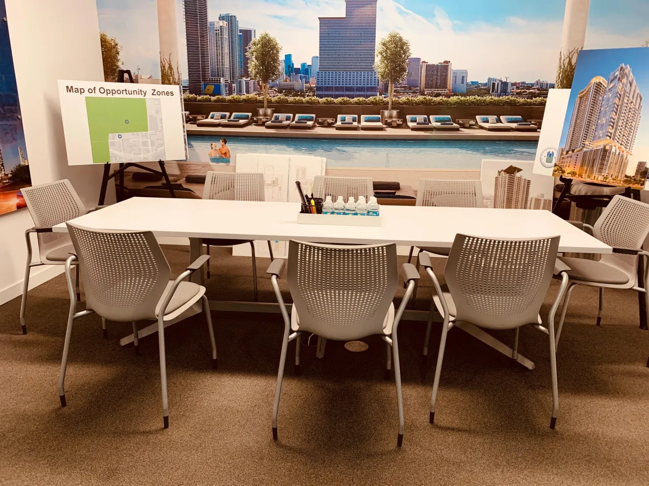 Small meeting/breakout area staged with marketing signage boards including a map and city renderings, white conference table with mesh chairs