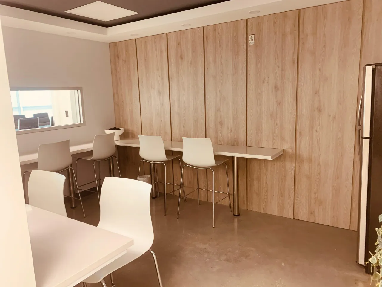 Breakroom with a light wood paneled wall, a narrow floating counter with bar stools, and a stainless refrigerator to the side