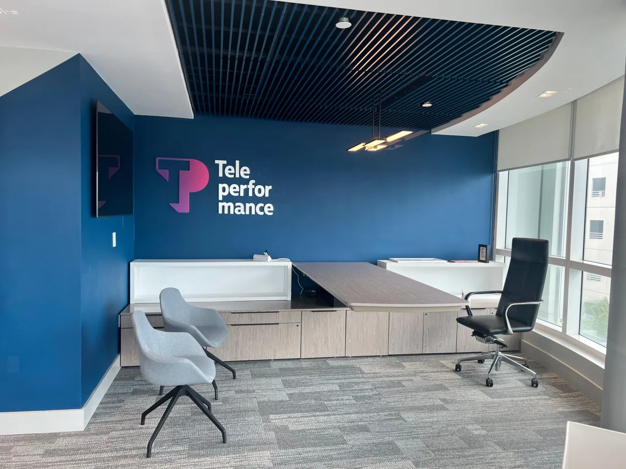 Executive office with a wood-grain desk and credenza run against a blue accent wall, a slatted ceiling feature, a task chair and two guest chairs