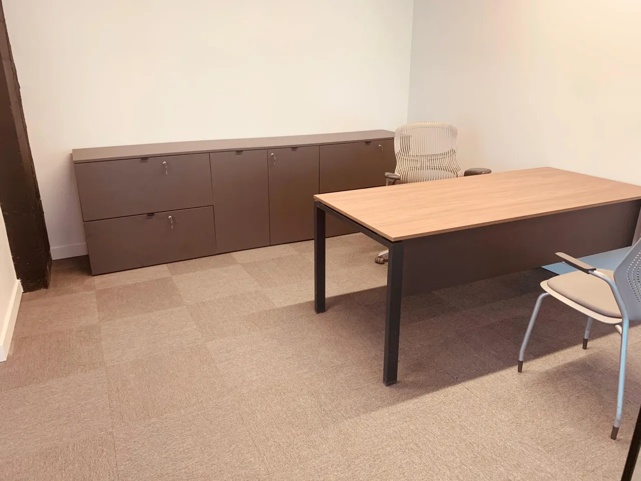 Private office with a wood-grain desk on a dark metal frame, a dark lateral credenza run with locking drawers, task and guest chairs on carpet tile