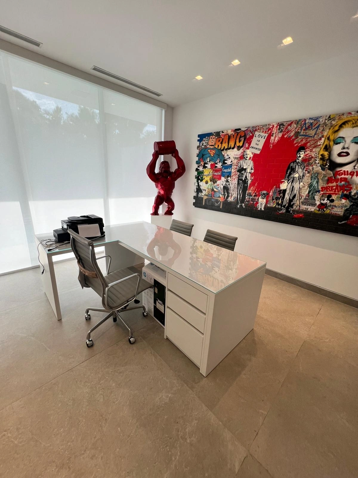 Home office with a white glass-topped desk over a three-drawer pedestal, a matching white side return holding a printer, and sheer-screened glazing