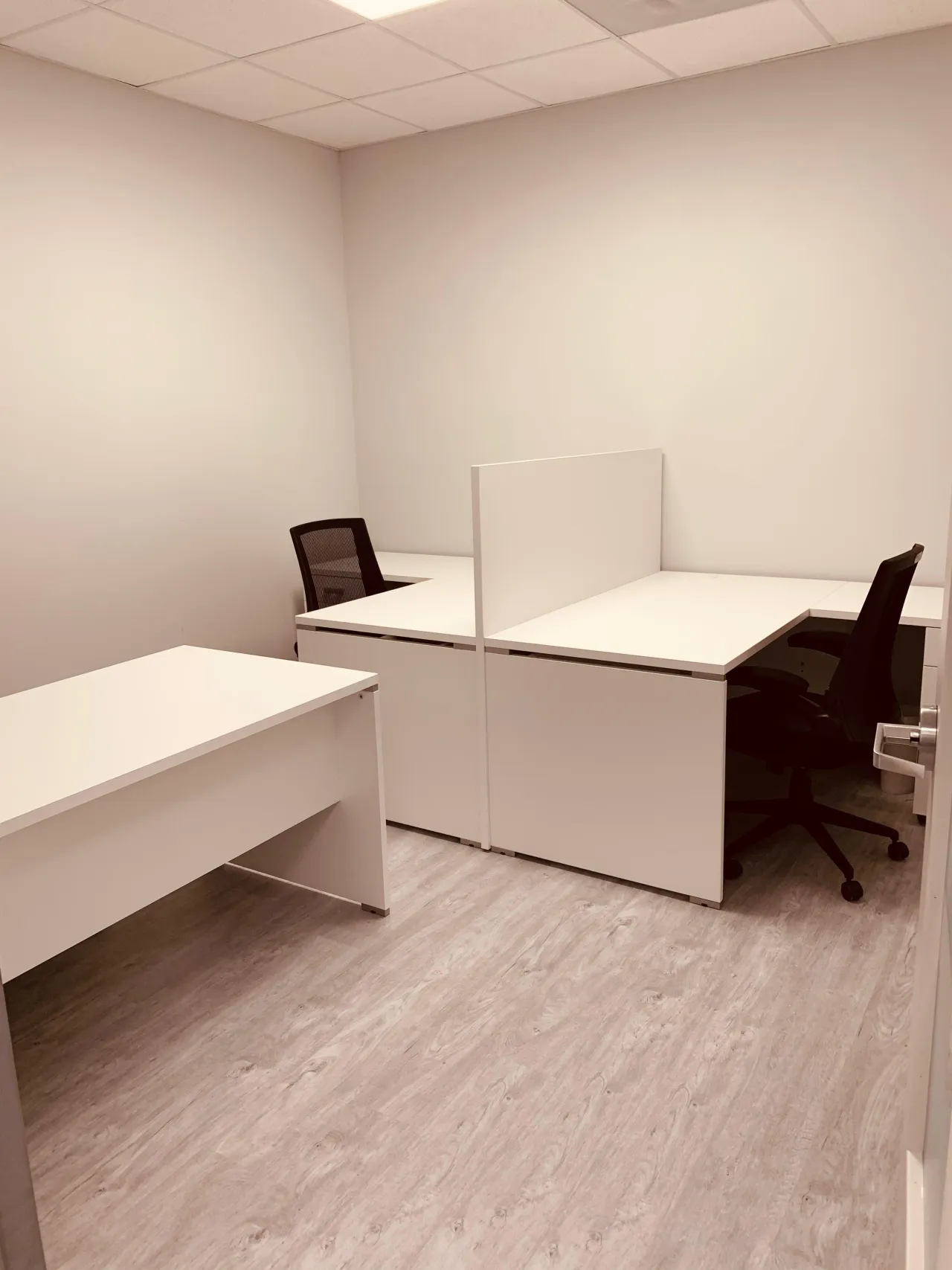 Small office with two white melamine desks set back to back, a white privacy panel between them, black mesh task chairs and a third desk on the wall