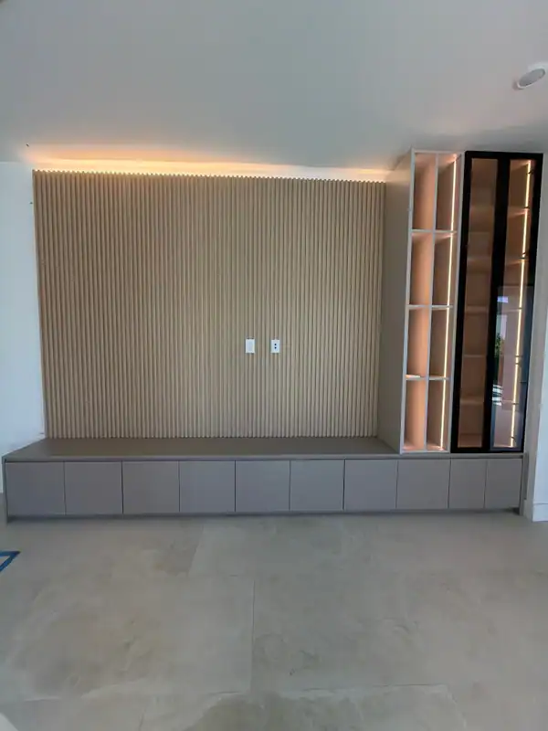Wood-grain slat wall with cove lighting above a long low cabinet bench, backlit white cubby shelving and a black-framed glass cabinet at right