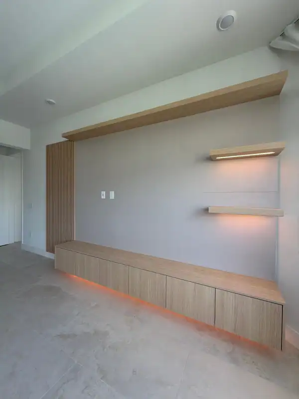 Media wall seen at an angle, low wood-grain cabinet with orange underlighting, two lit floating shelves, wood-grain header and slat panel at left
