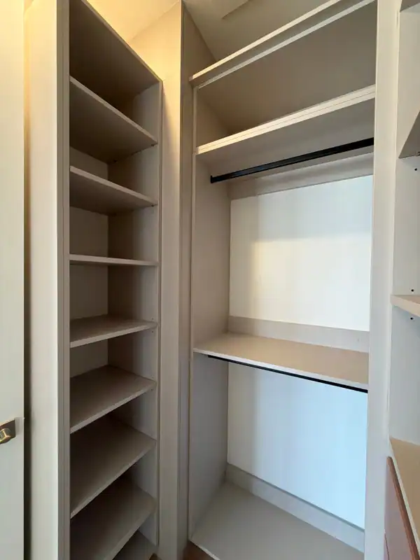 Closet corner with a tall open shelf tower at left and two stacked black hanging rods with a shelf between them, greige panels