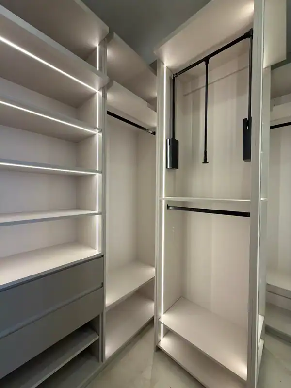 Walk-in closet with LED-lit shelves and drawers at left and a tall unit at right holding a pull-down rod above a fixed hanging rod
