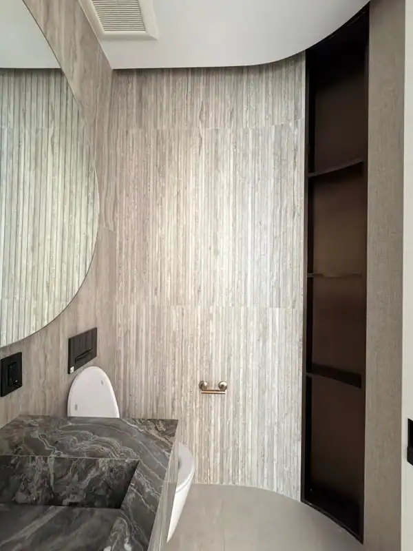 Vertical striated stone-look wall tile with a dark veined stone vanity edge, a wall-hung toilet, and a recessed dark open shelf niche