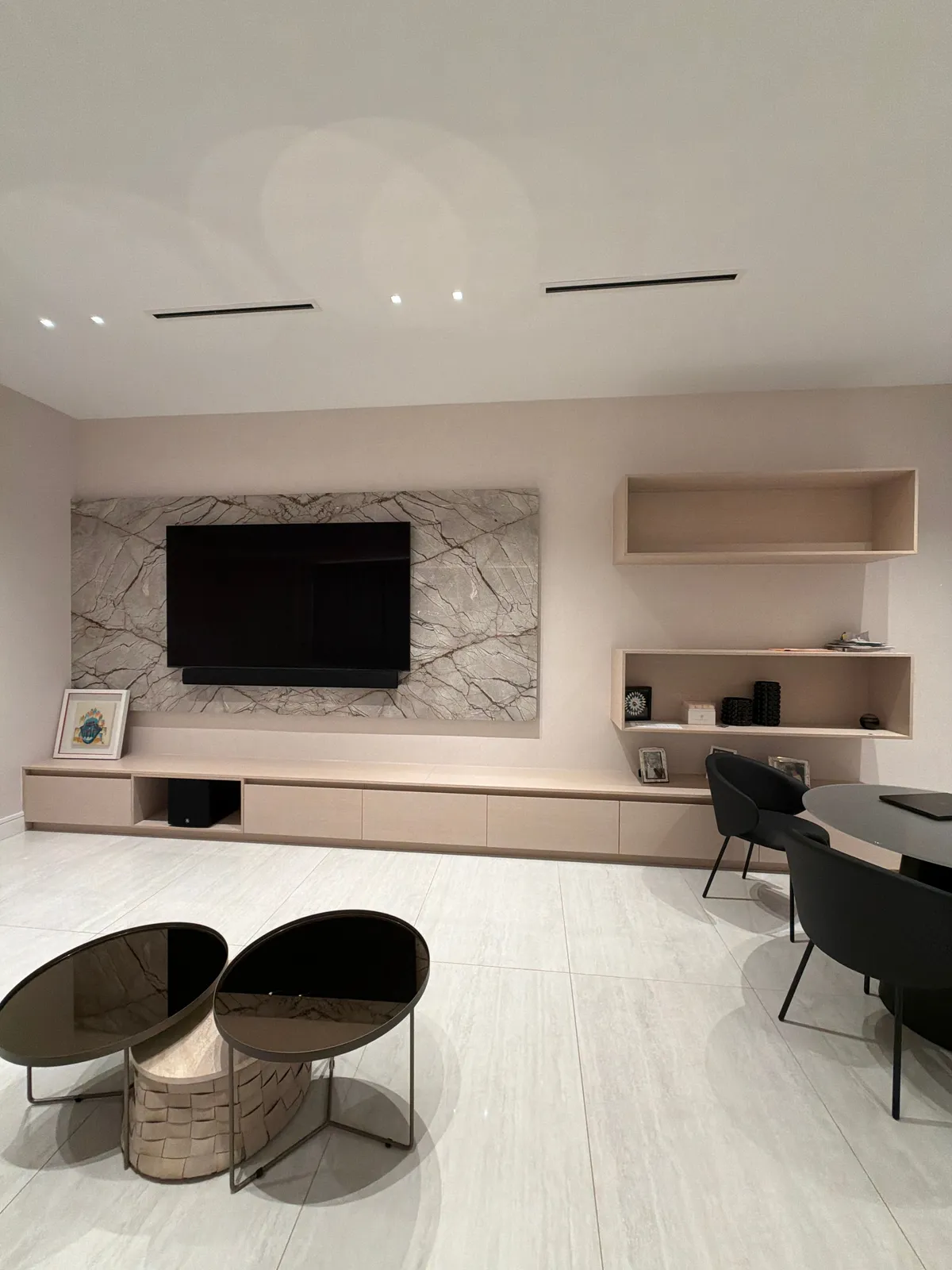 Veined stone wall behind a mounted TV above a long low wood-grain credenza, with two open wood-grain shelf boxes on the wall to the right