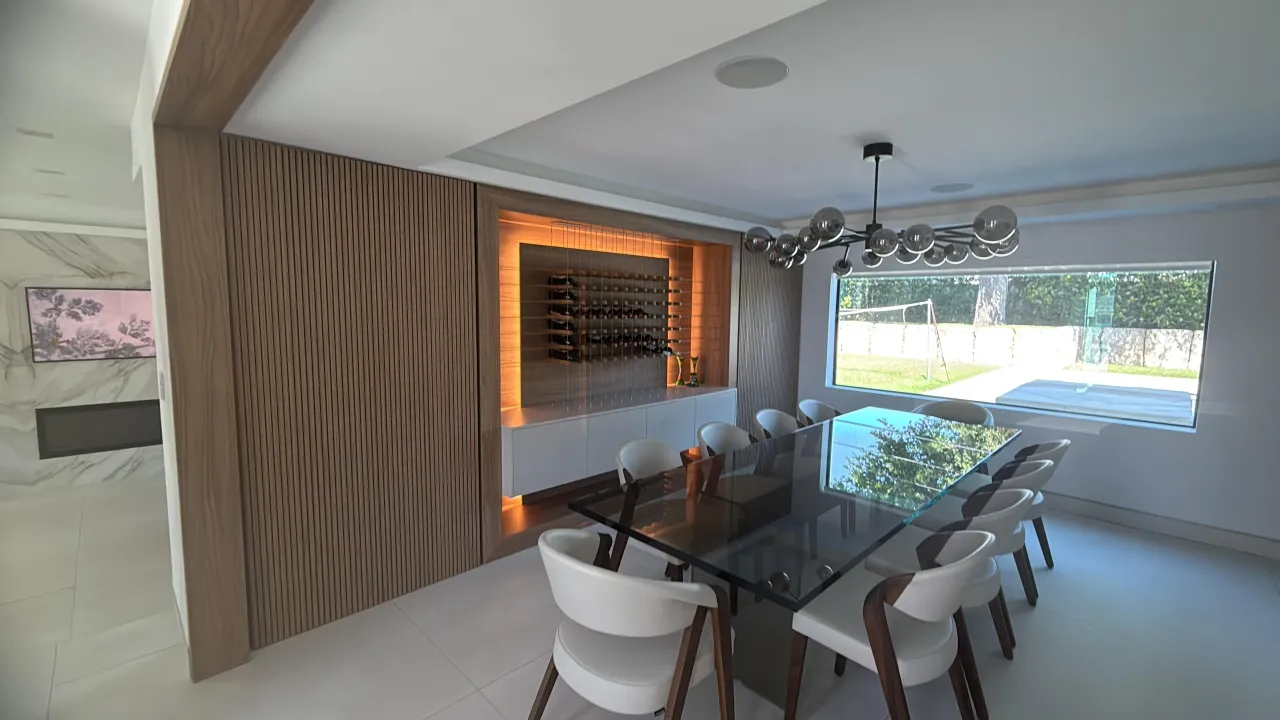 Built-in wine rack with orange backlighting set into a wood slat wall, beside a glass-top dining table and chrome bubble chandelier