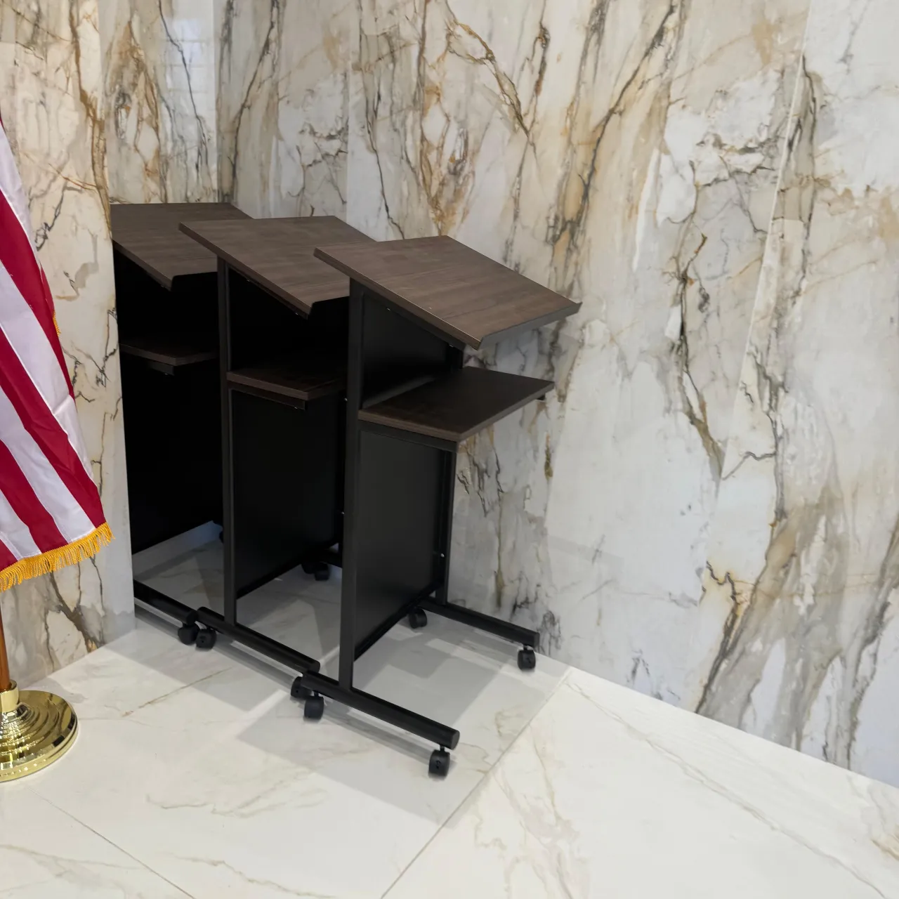 Three dark wood-topped rolling podiums with black metal frames and casters, staged against a large veined stone wall