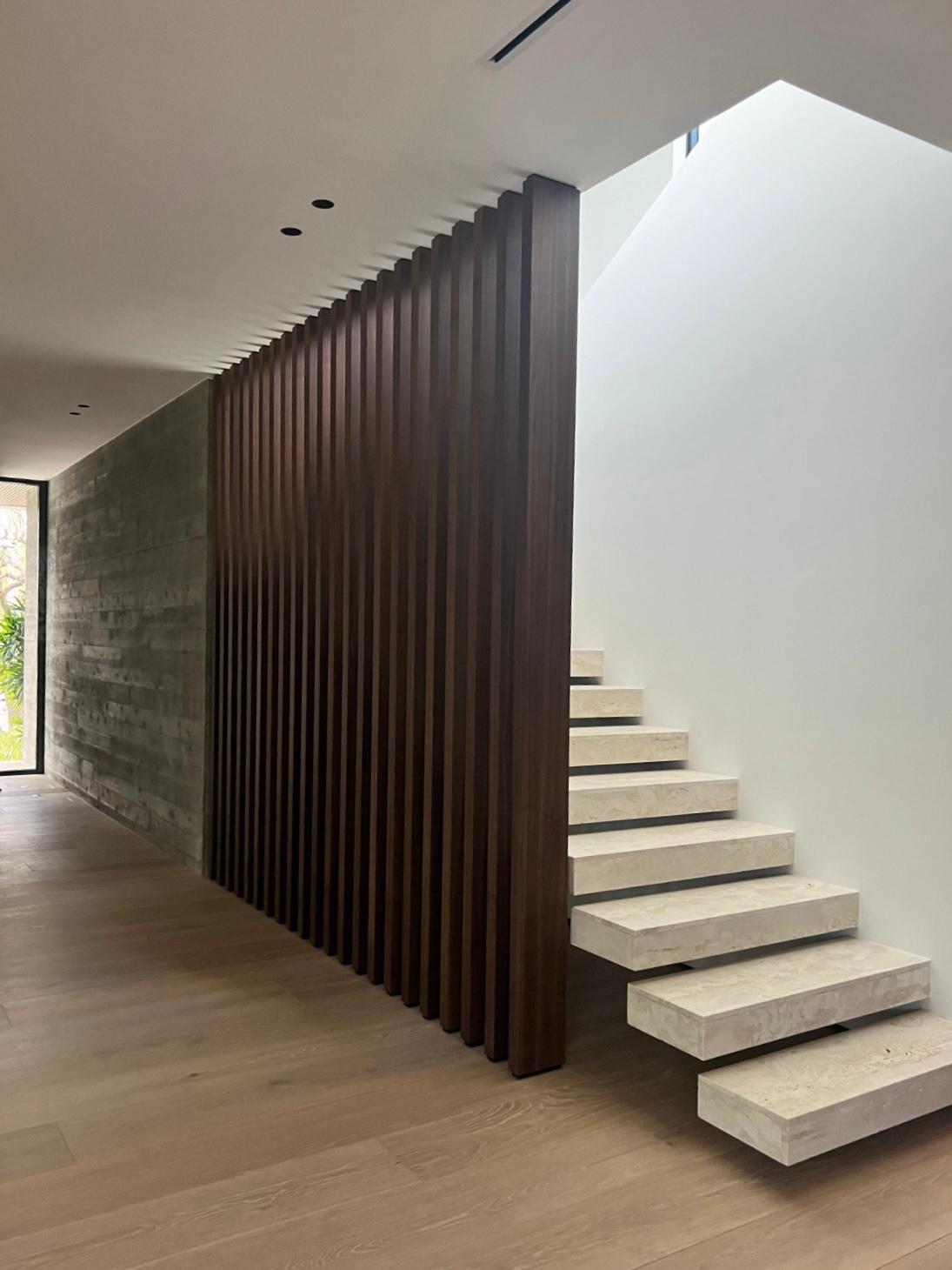 Dark wood vertical slat wall wrapping a corner beside a board-formed concrete wall, next to a floating stair with pale stone treads on light wood floor