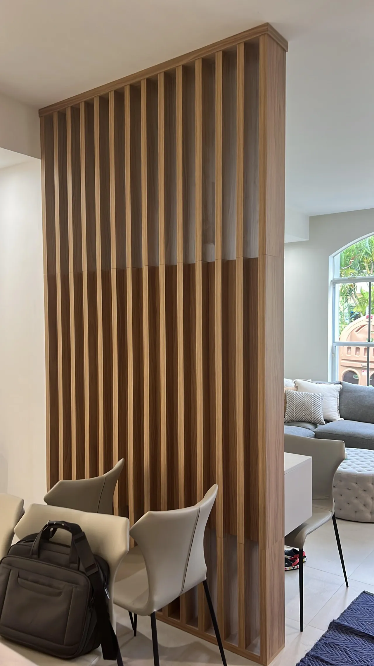 Floor-to-ceiling wood vertical slat room divider separating a living area, with a sofa lounge on one side and dining chairs on the other
