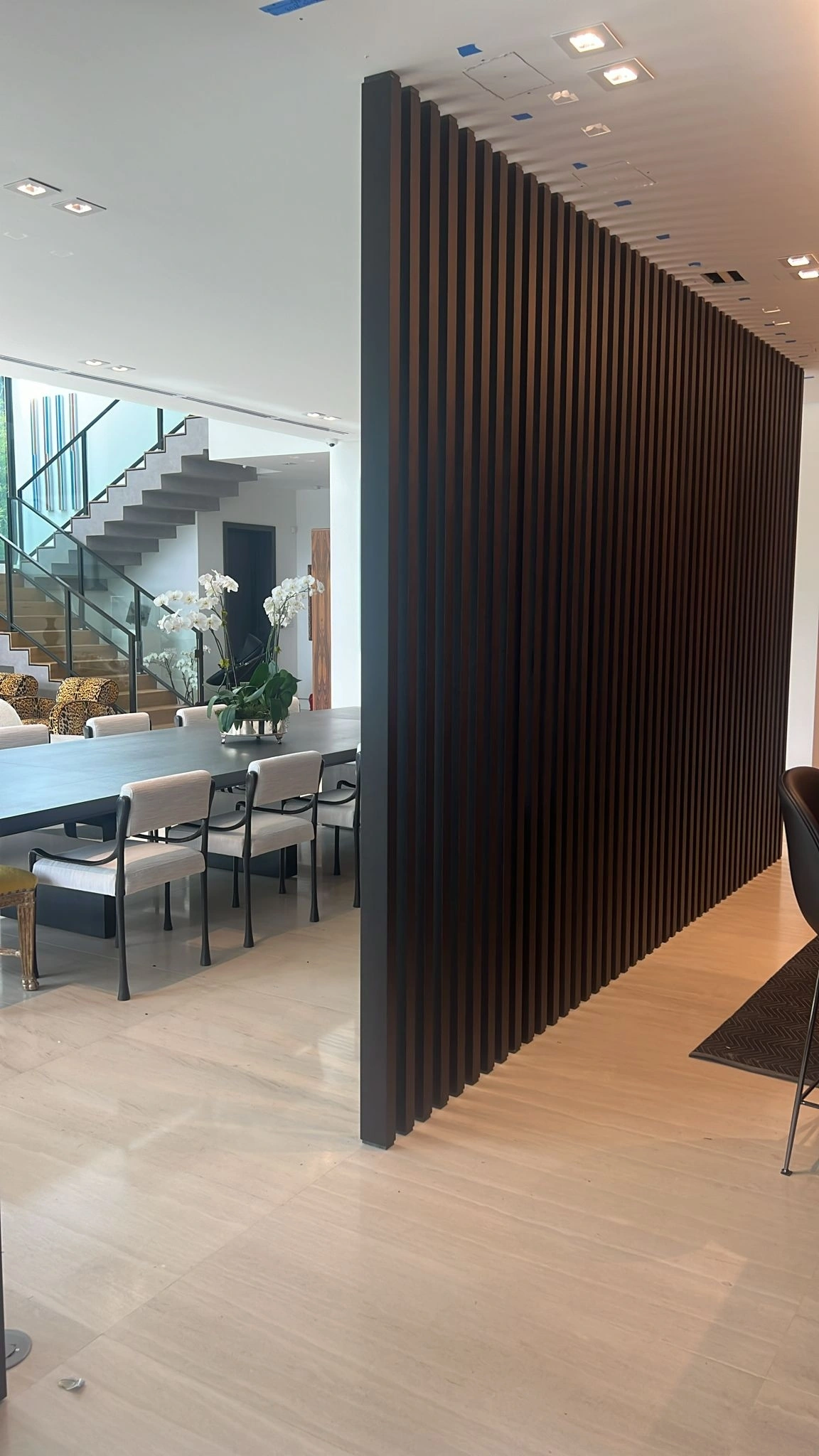 Freestanding dark wood vertical slat room divider between a dining area and a living space with a staircase, veined stone floor throughout