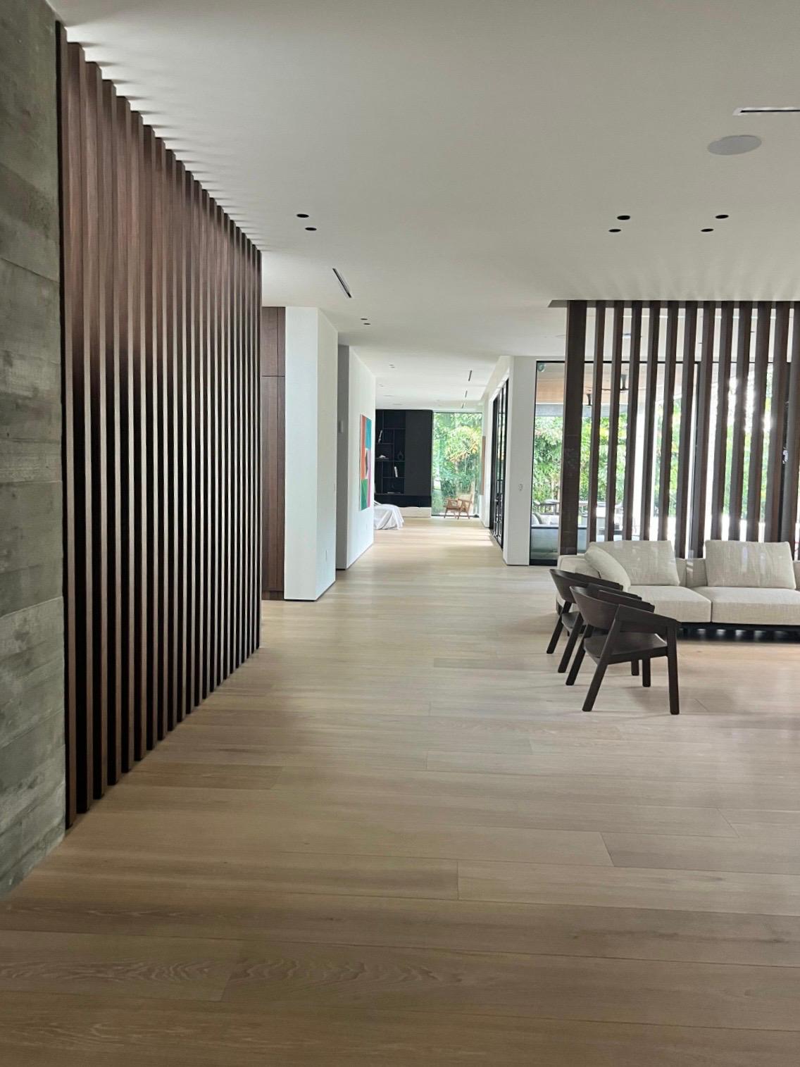 Long hallway with a floor-to-ceiling dark wood slat wall at left, a second slat screen at right beside cream seating, light wood floor throughout