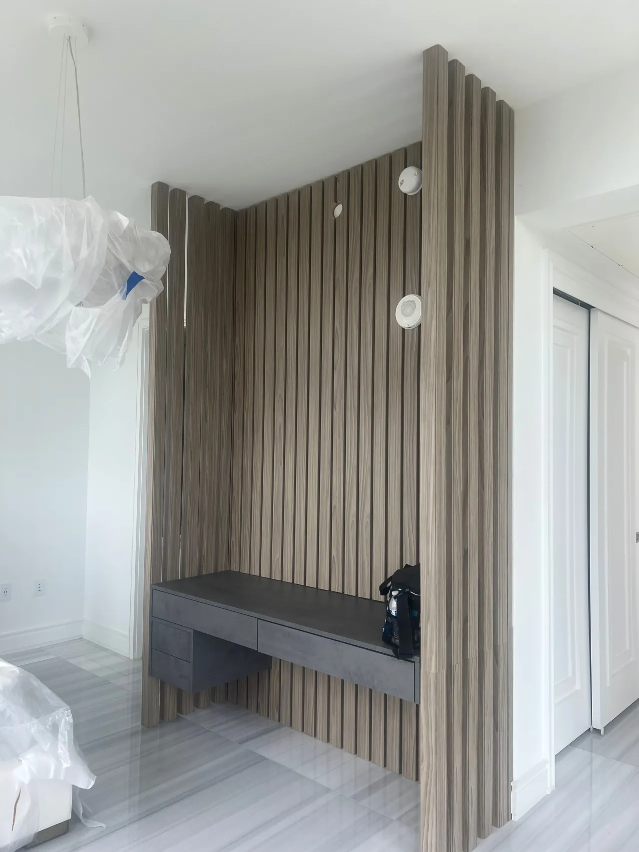 Wood vertical slat wall enclosure with a dark gray floating vanity desk built into the base, closet door visible to the side