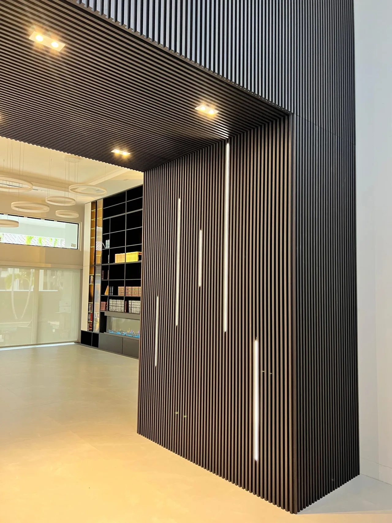 Black vertical fluted wall and ceiling feature wrapping a corner, with integrated vertical LED light strips in a tiled lobby-like space
