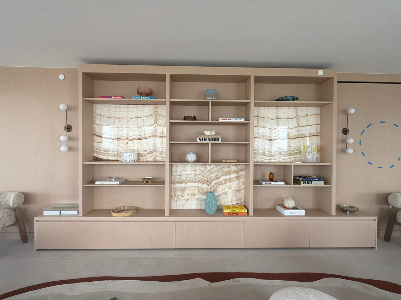 Custom-stained wood veneer display wall with open shelving, backlit banded stone-look panels behind the niches, and a long floating drawer run below