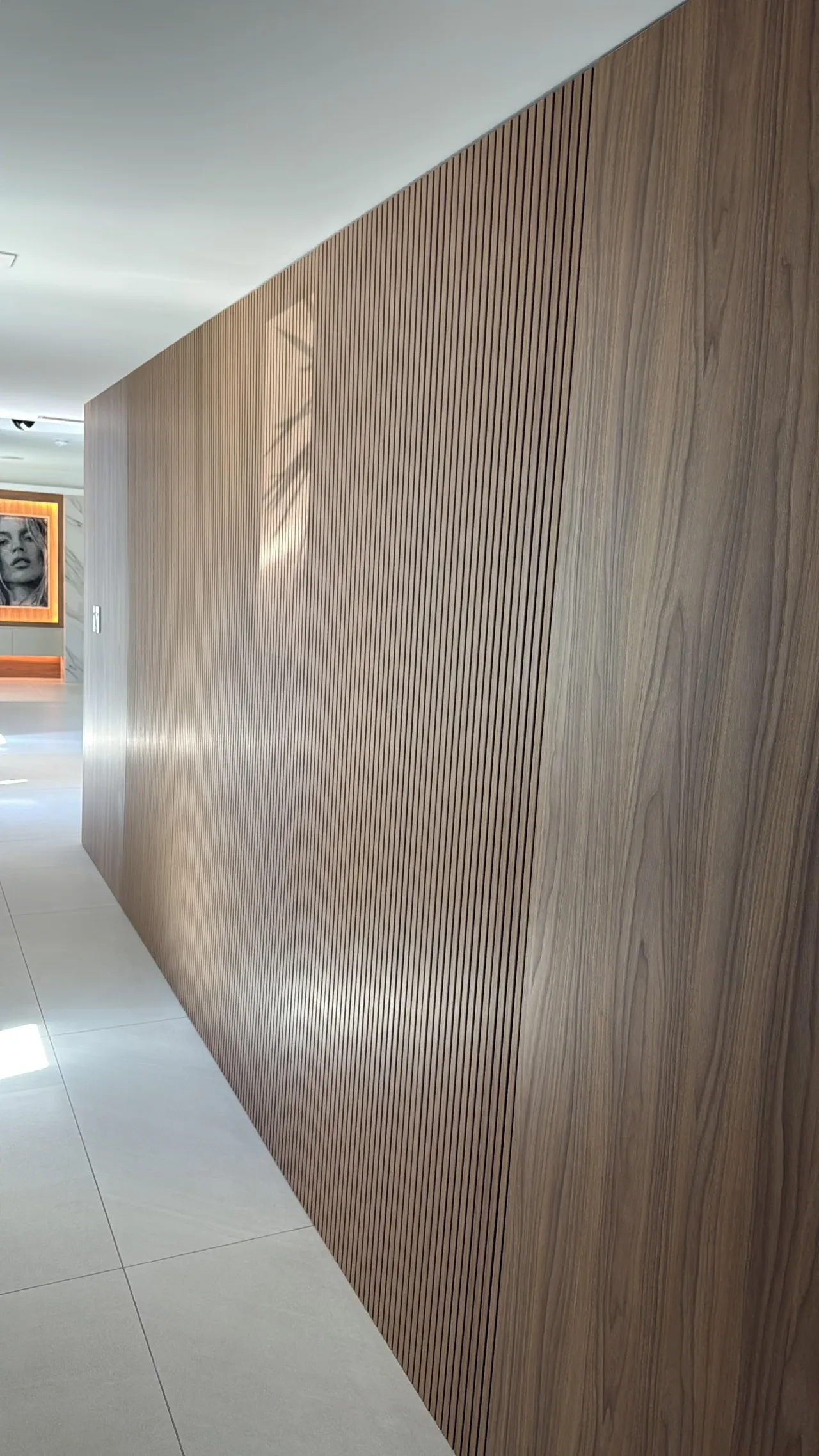 Dark wood-grain fluted vertical panel wall in a hallway with a framed portrait artwork on the adjacent wall, polished light floor
