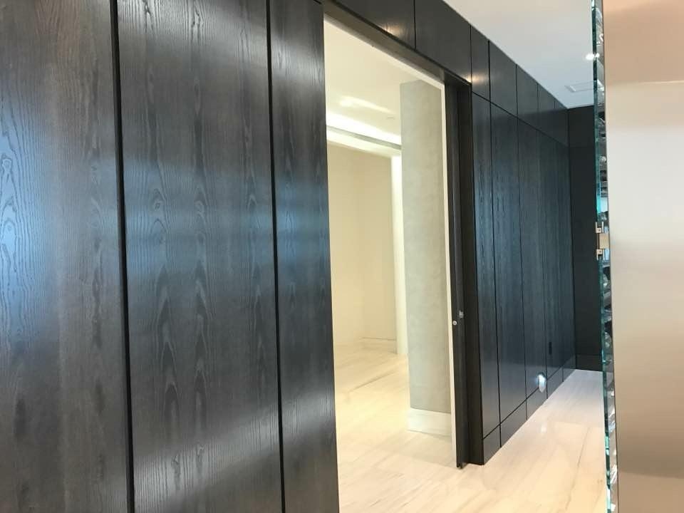 Dark wood-grain paneled wall run with a wide opening to a bright white passage, pale stone plank floor, glass display unit at right