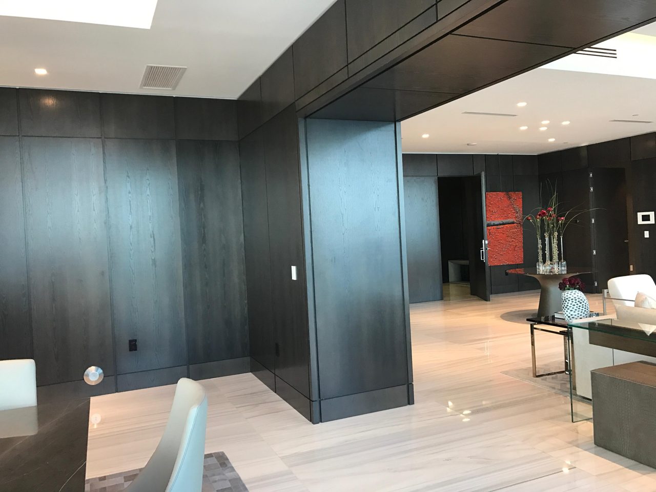 Dark wood-paneled corner with a structural column wrap, open sliding door leading to a red-accented room, veined stone floor