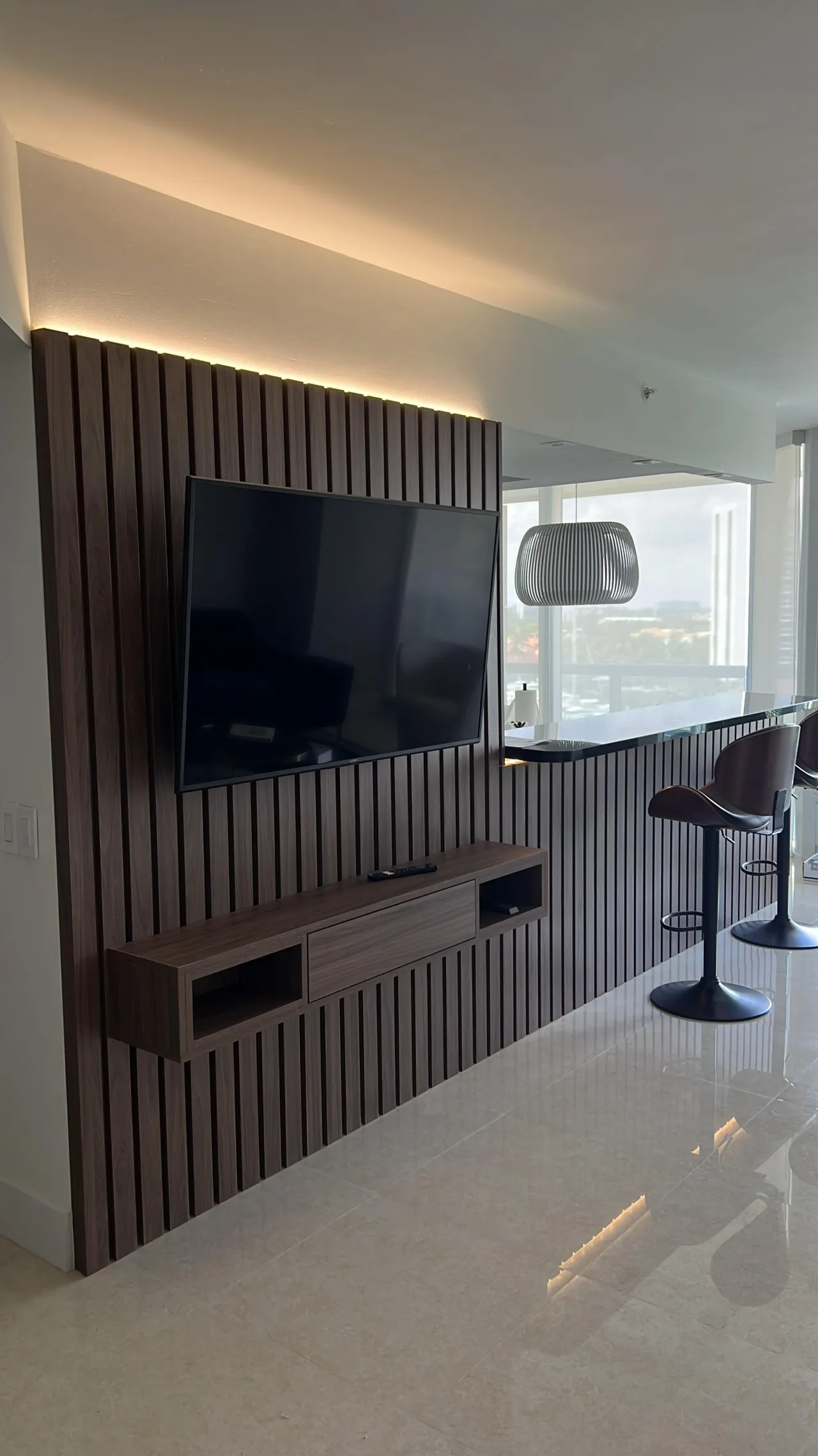 Dark wood vertical slat accent wall with a wall-mounted TV and a floating dark wood media console, integrated LED backlight above