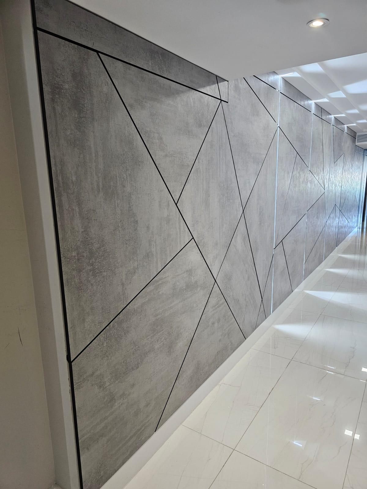 Gray concrete-look panels with black inlay lines in angular shapes, seen down a corridor, with a dark edge trim and glossy white veined tile floor