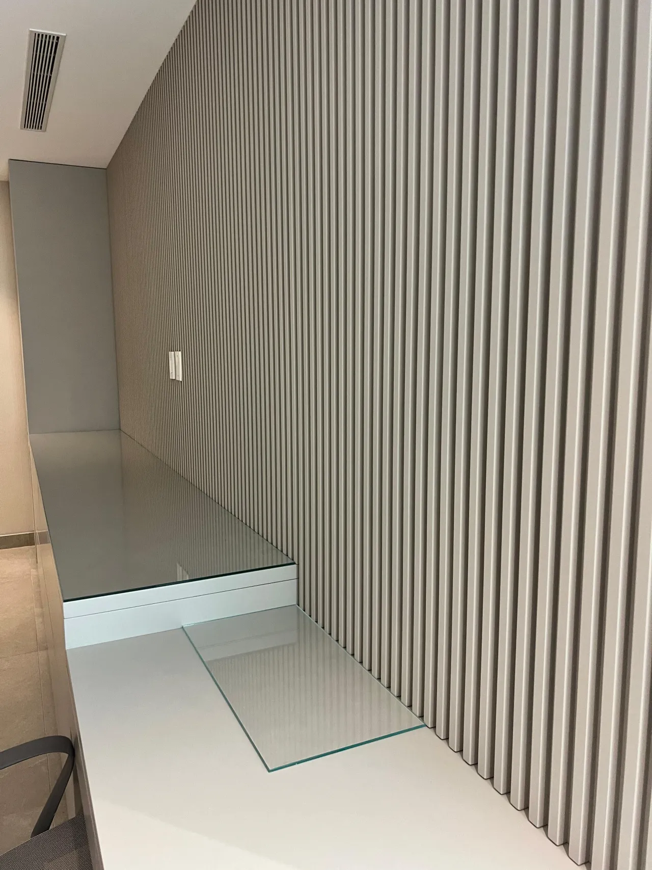 Gray fluted vertical wall paneling in a small office nook with a glass desktop and glass shelf surfaces, mirror panel at left