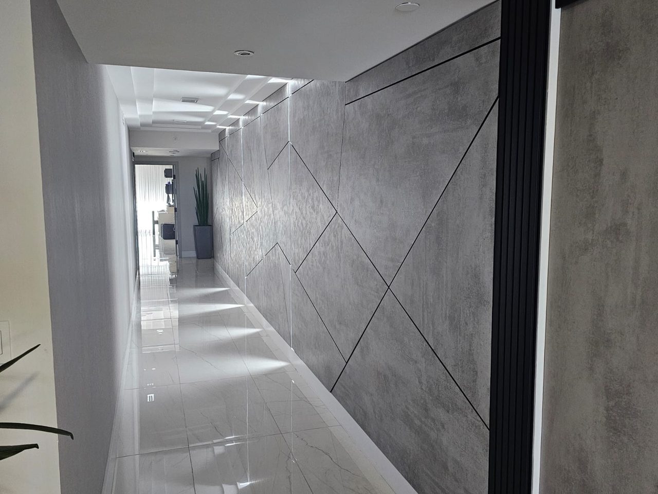 Gray geometric concrete-look panel wall with black fluted trim strip at corner, single vertical LED strip, coffered ceiling