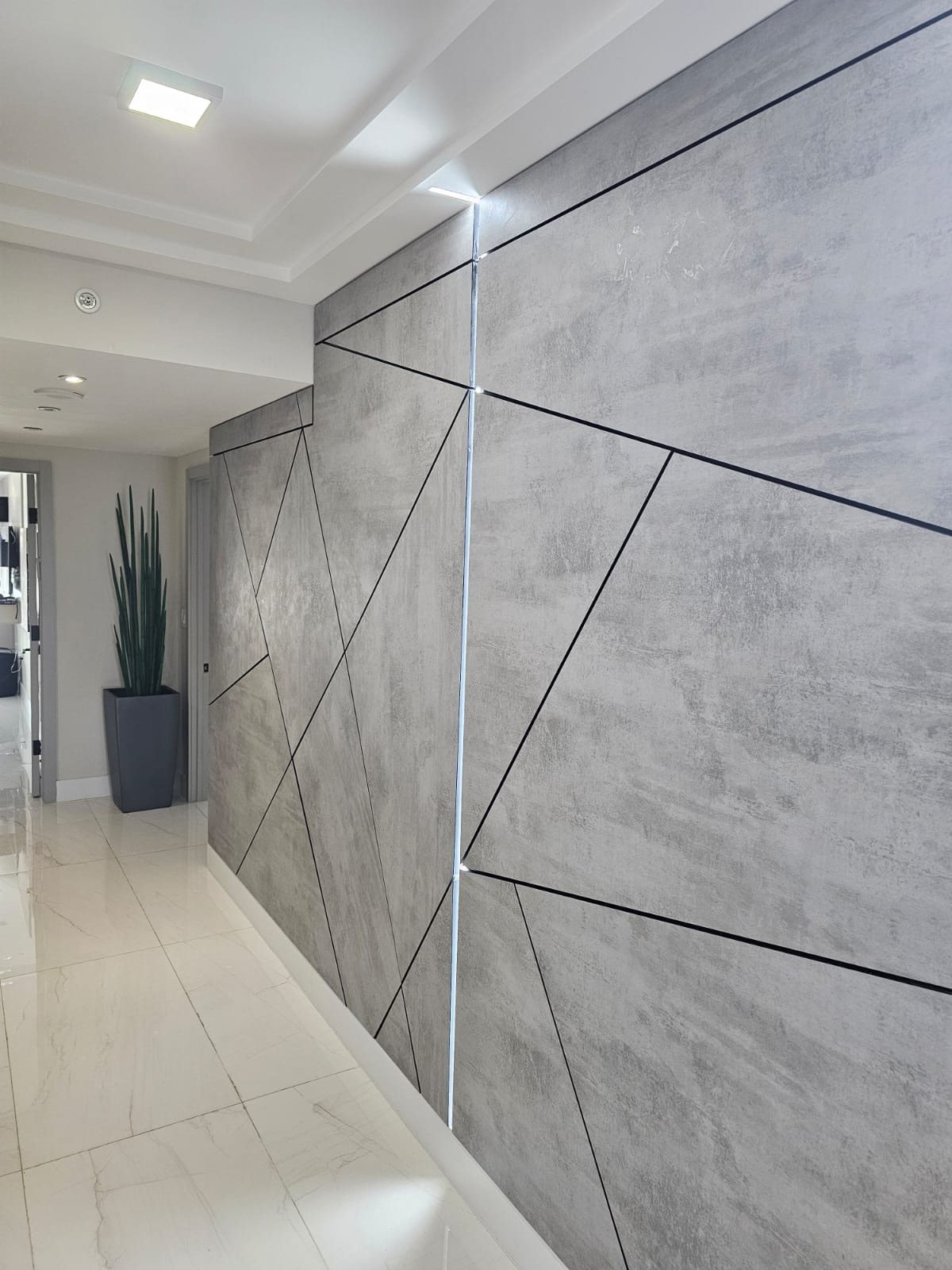 Gray geometric concrete-look panel wall with a step-down section and vertical LED strip lighting, potted plant nearby