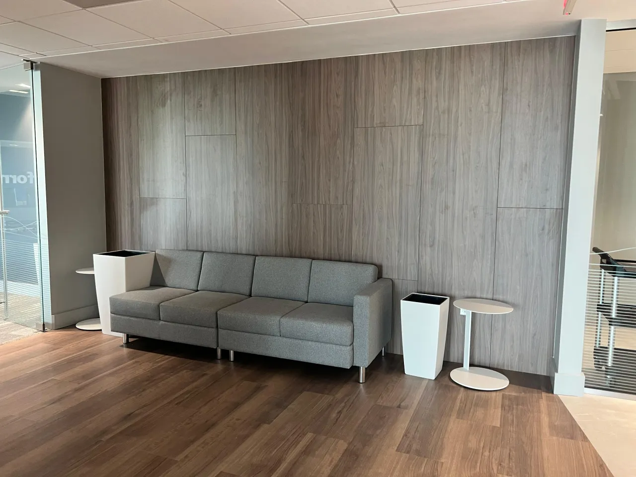 Gray wood plank paneling in a commercial lobby behind a gray fabric sofa, with tall white planters and dark wood flooring