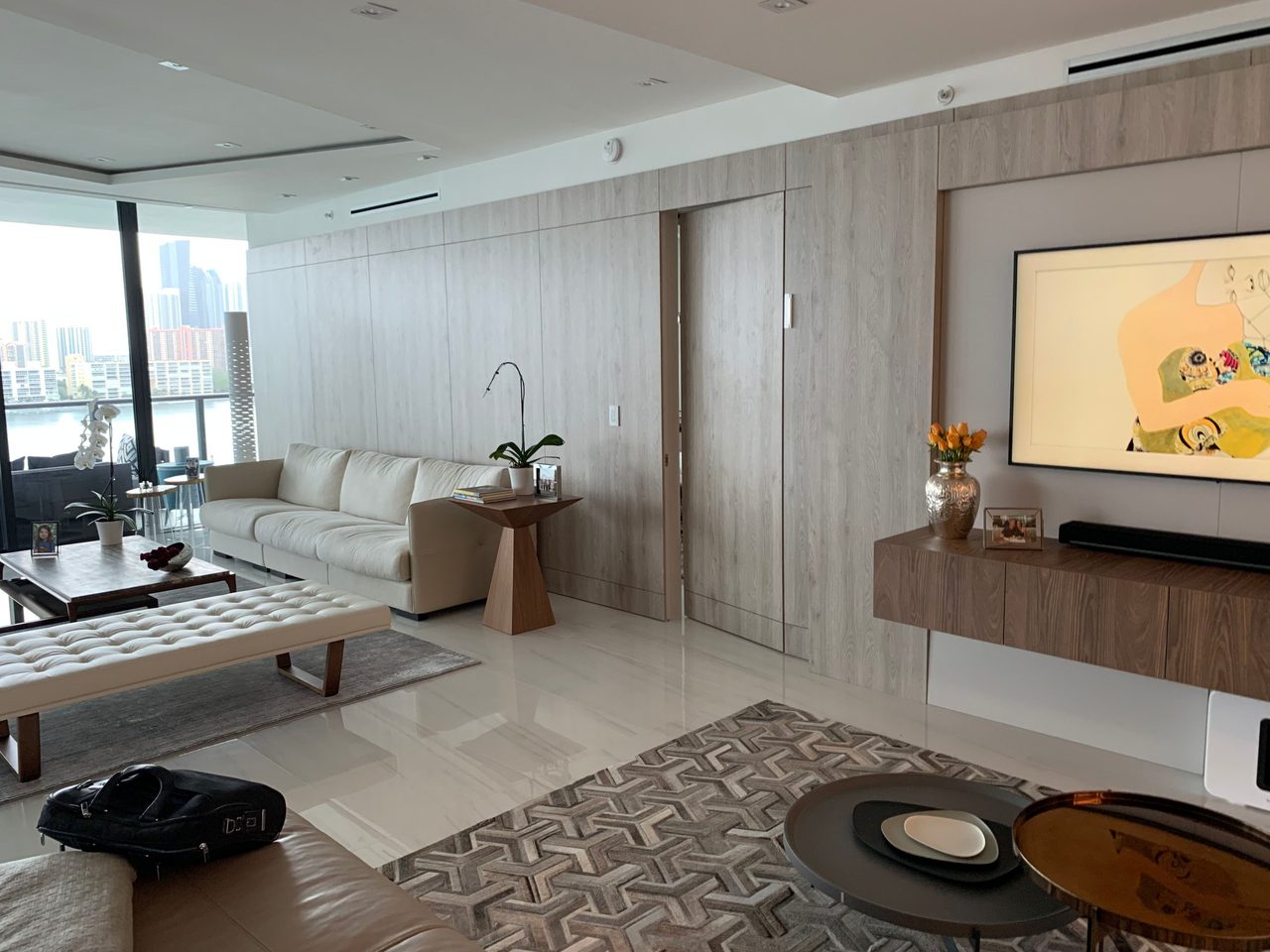 Light gray wood-grain paneled wall with flush closet doors and a wall-mounted TV over a floating console, cream sofa and leather-look sectional in view