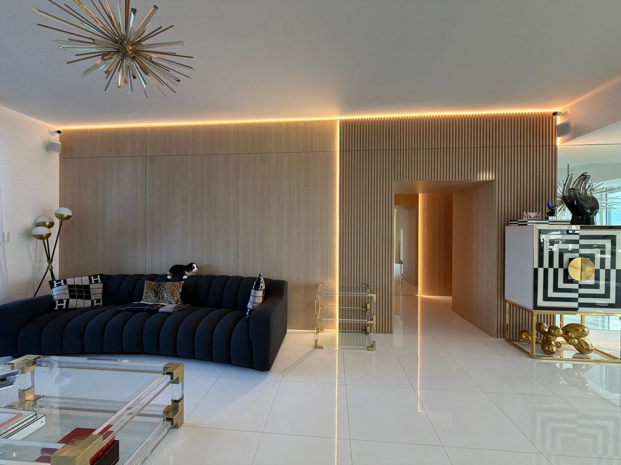Light wood-grain flat-panel wall meeting a vertical slat section with a recessed cove line and a paneled hallway opening beside a black-and-white cabinet