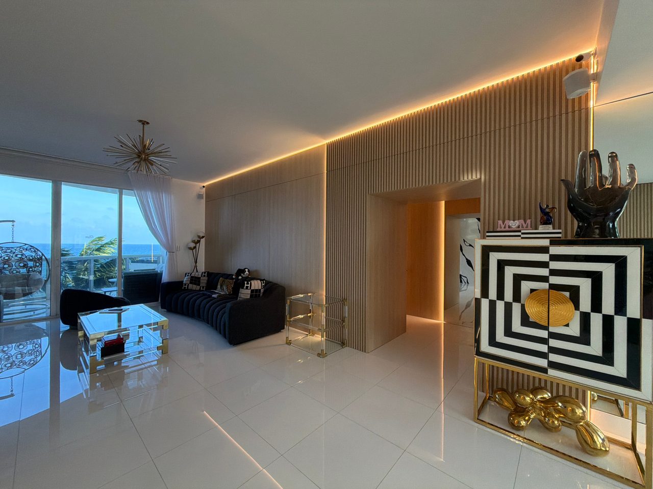 Living room wall of light wood-grain vertical slats and flat panels with warm cove lighting, framing a paneled passage to the hallway