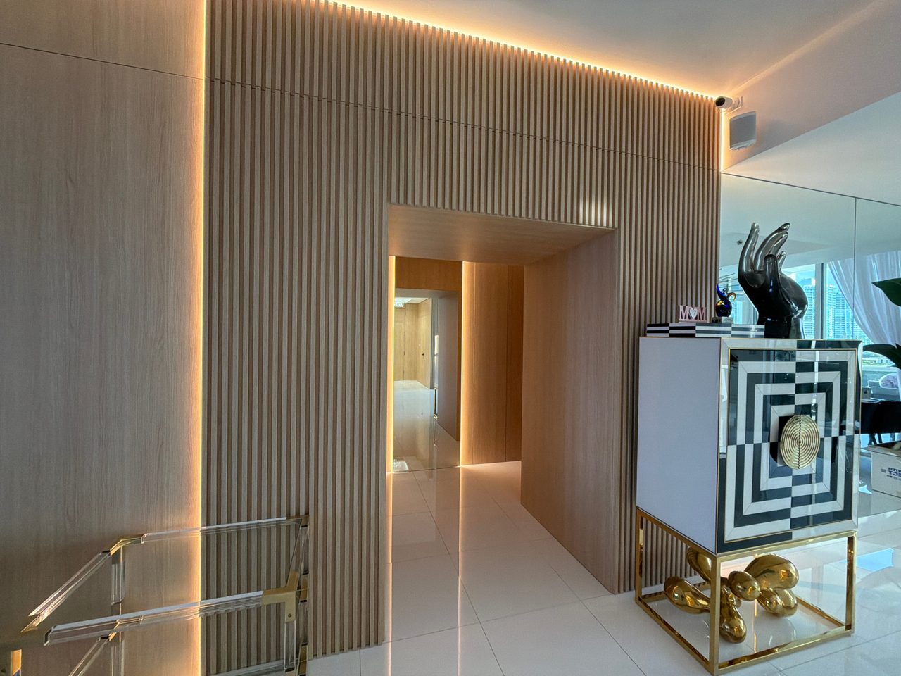 Floor-to-ceiling light wood-grain vertical slats with cove lighting along the ceiling line and a paneled hallway opening