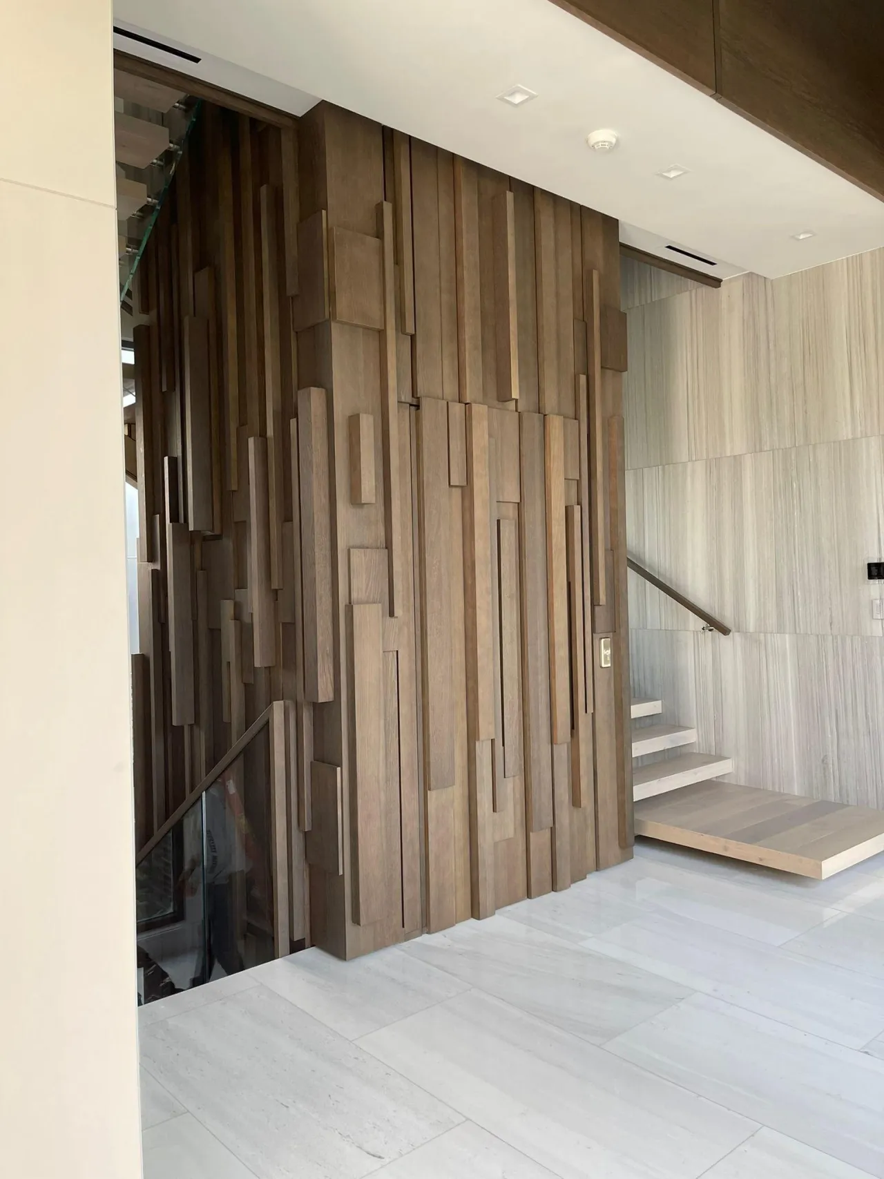 Sculptural three-dimensional wood block feature wall wrapping an entry corner with staggered vertical wood fins of varying heights