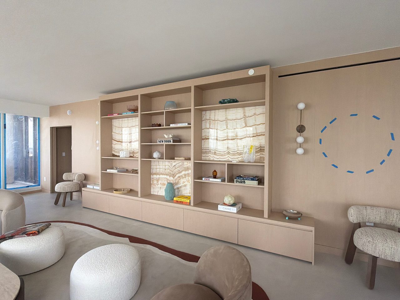 Custom-stained wood veneer display wall seen at an angle, open shelves over backlit stone-look panels, floating drawer run below, paneled wall beyond