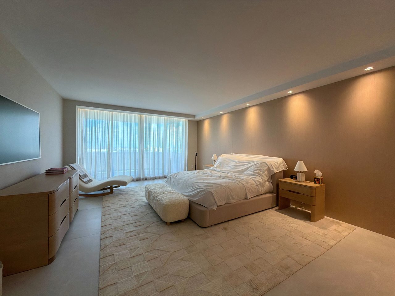 Bedroom with a full-height custom-stained wood veneer headboard wall washed by recessed downlights, a wood-grain nightstand and a curved veneer dresser