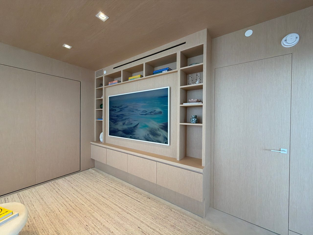 Custom-stained wood veneer media unit with open display shelving and a floating four-drawer base, set between full-height paneled walls and a flush door