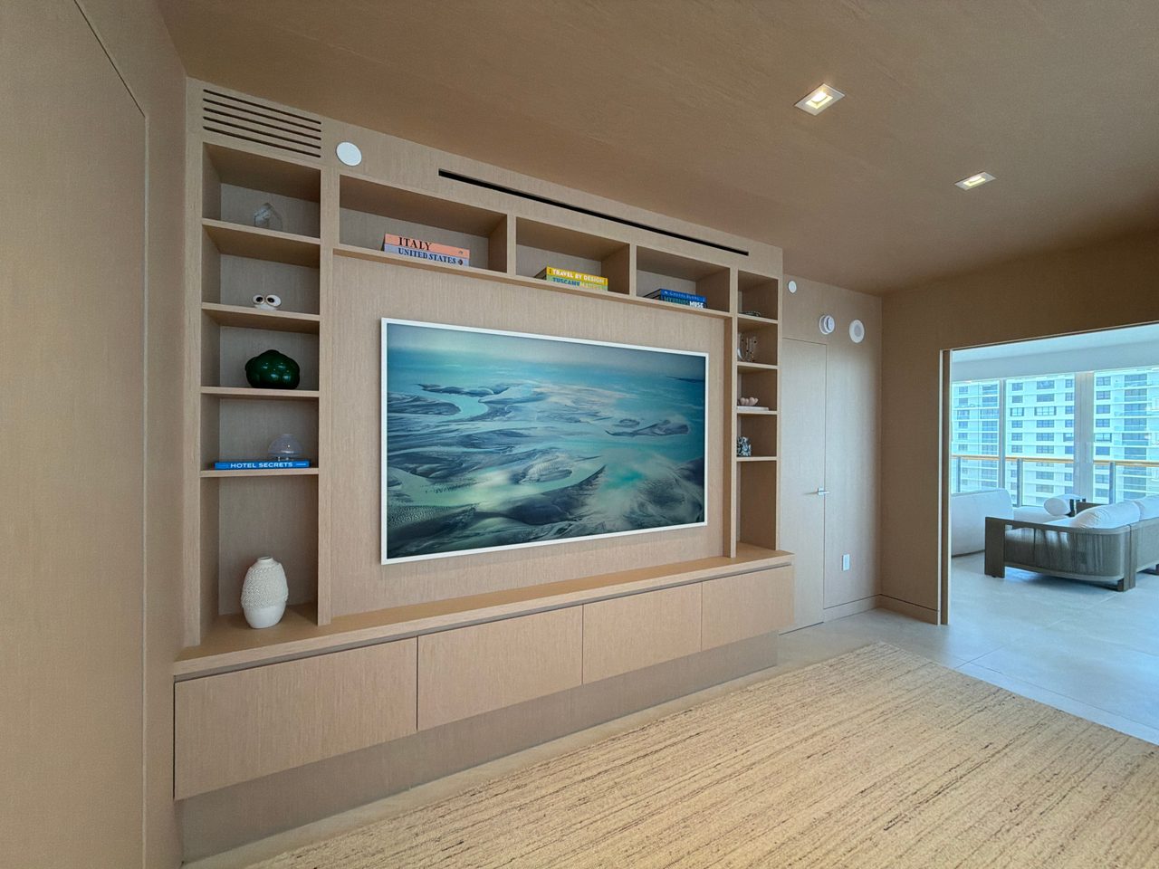 Custom-stained wood veneer media wall at an angle, open shelving columns flanking a recessed screen panel over a floating cabinet run, paneled wall beyond