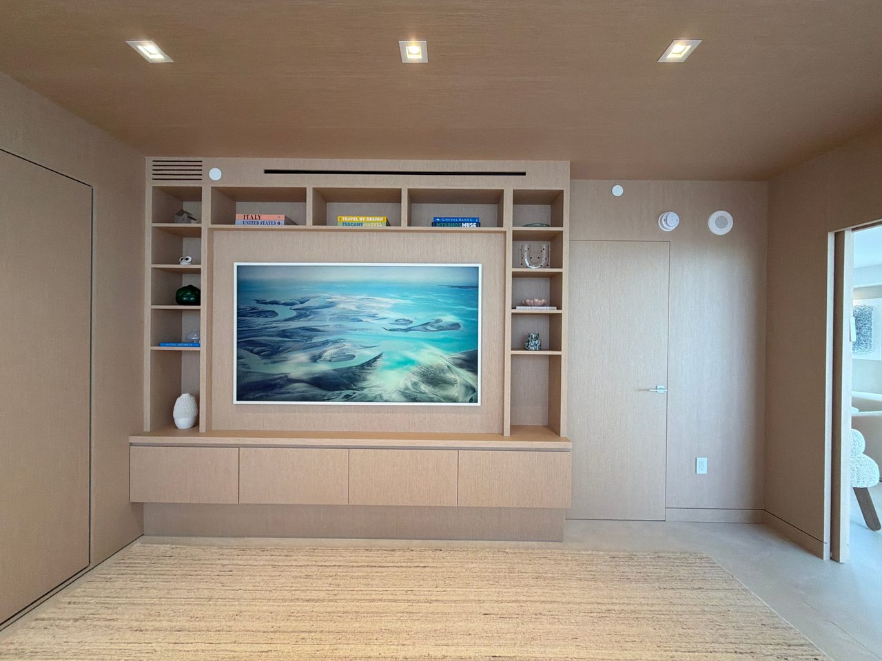 Custom-stained wood veneer media wall with an open shelf grid framing a recessed screen panel, floating four-door base cabinet and matching wall paneling