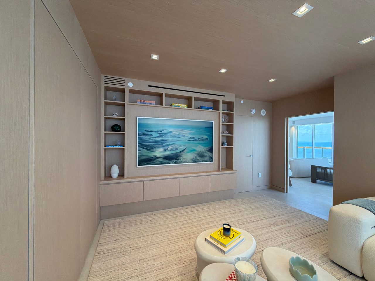 Full-height custom-stained wood veneer wall paneling running to a built-in media unit with open shelving and a floating cabinet run, doorway to a sea view