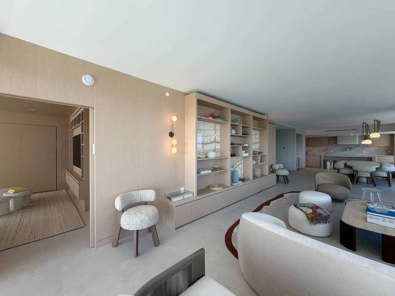Full-height custom-stained wood veneer built-in shelving wall with backlit stone panels and a media niche, opening to the kitchen and dining area beyond