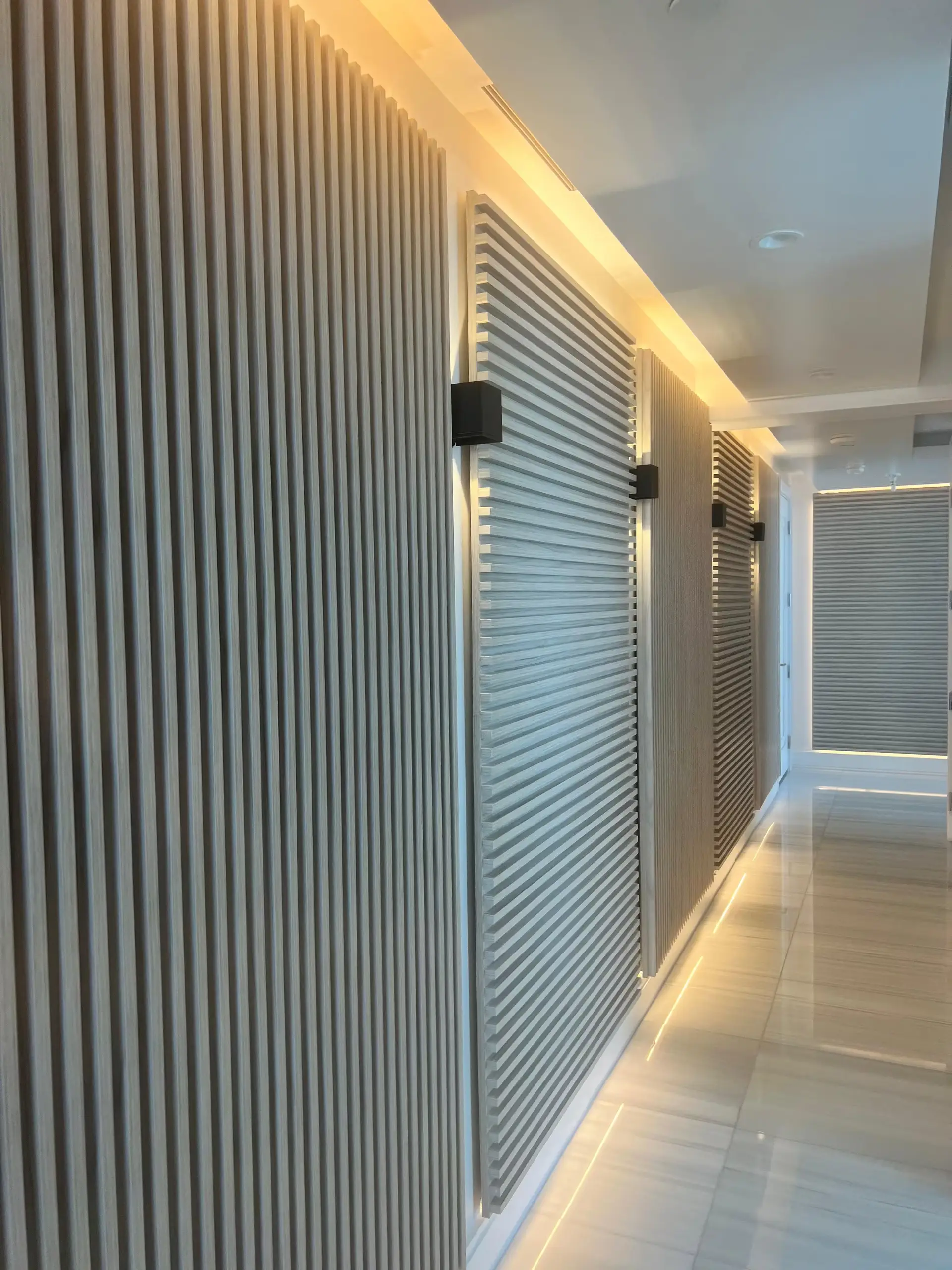 Corridor lined with vertical fluted wood slat panels, black sconces, and warm LED accent lighting